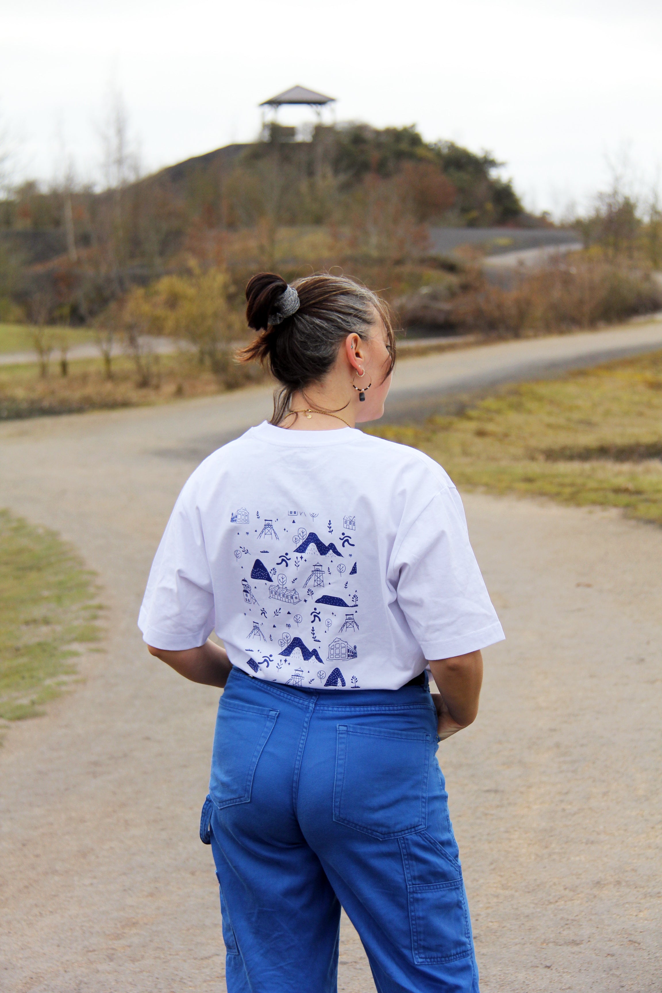 T-shirt unisexe blanc patrimoine minier porté de dos, illustration minière bleue au dos en extérieur